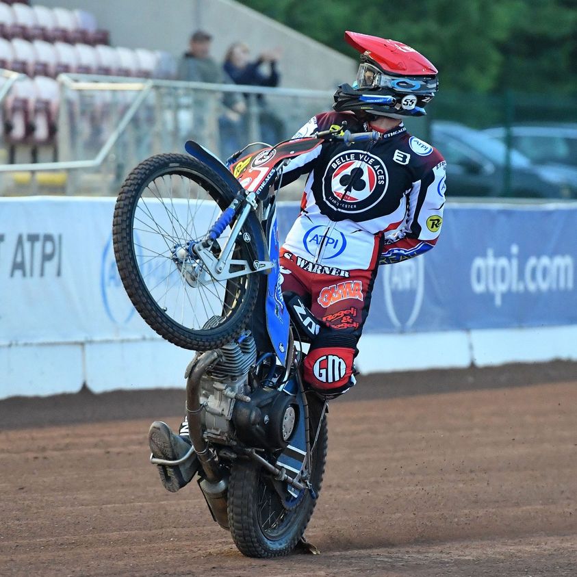 Speedway motorcycle rider in racing suit performing wheelie on dirt track