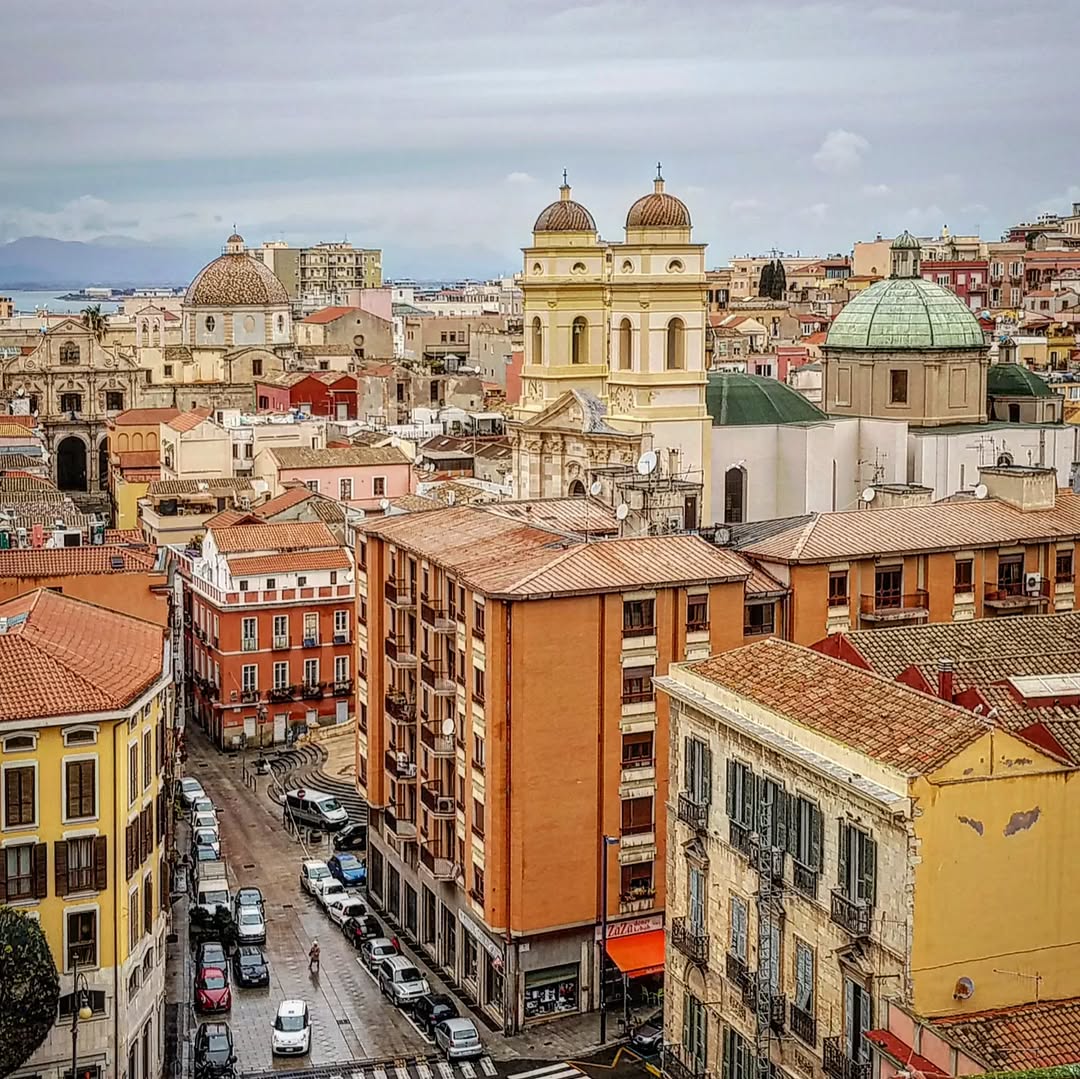 Aerial view of Cagliari, Italy with colorful buildings, church domes, and terracotta rooftops
