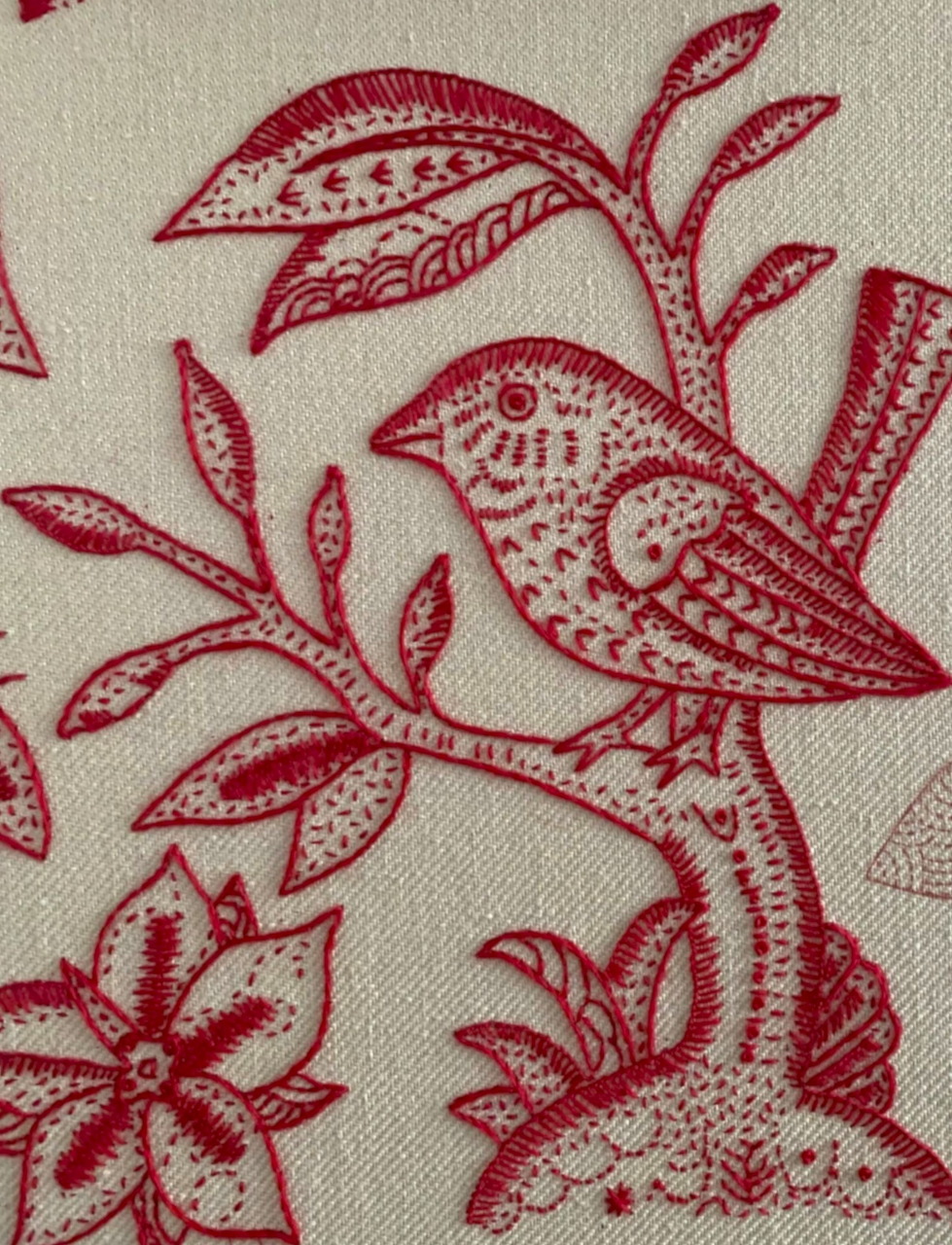 Red embroidered bird with ornate patterns on branch with leaves on beige fabric
