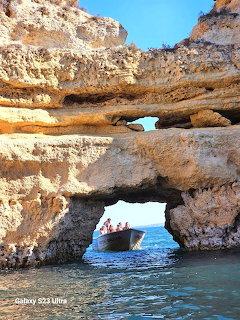 Tour boat passing through a natural limestone rock arch along a coastal cliff face