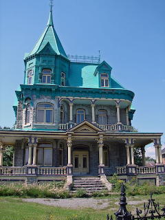 Historic Victorian mansion with turquoise roof and white wraparound porch on green lawn