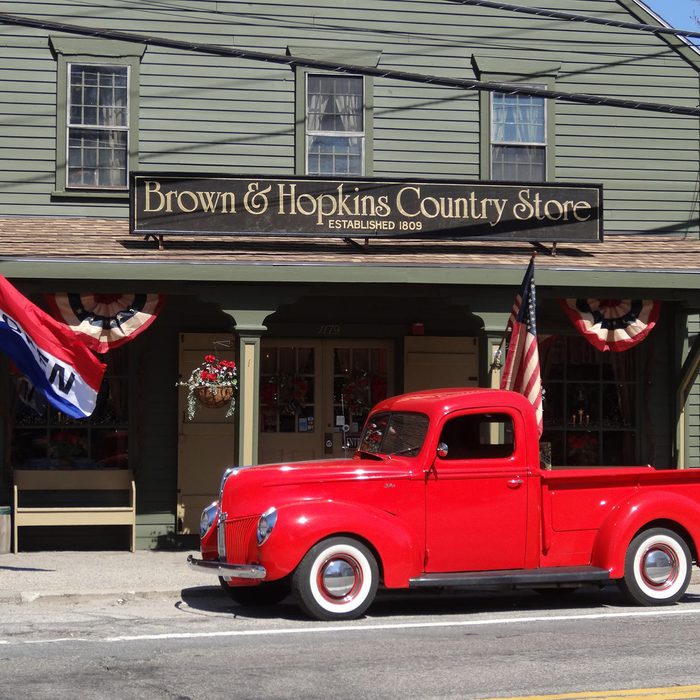 Red vintage pickup truck parked outside a country store with patriotic decorations