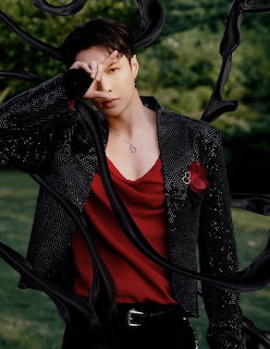 Portrait of a man in a black jacket and red shirt framed by dark branches outdoors