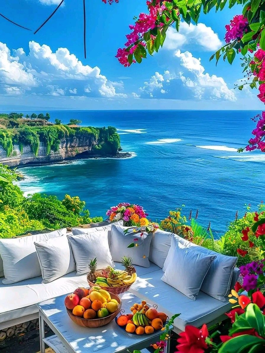 Terrace seating with fruit and flowers overlooking a blue ocean and coastal cliffs