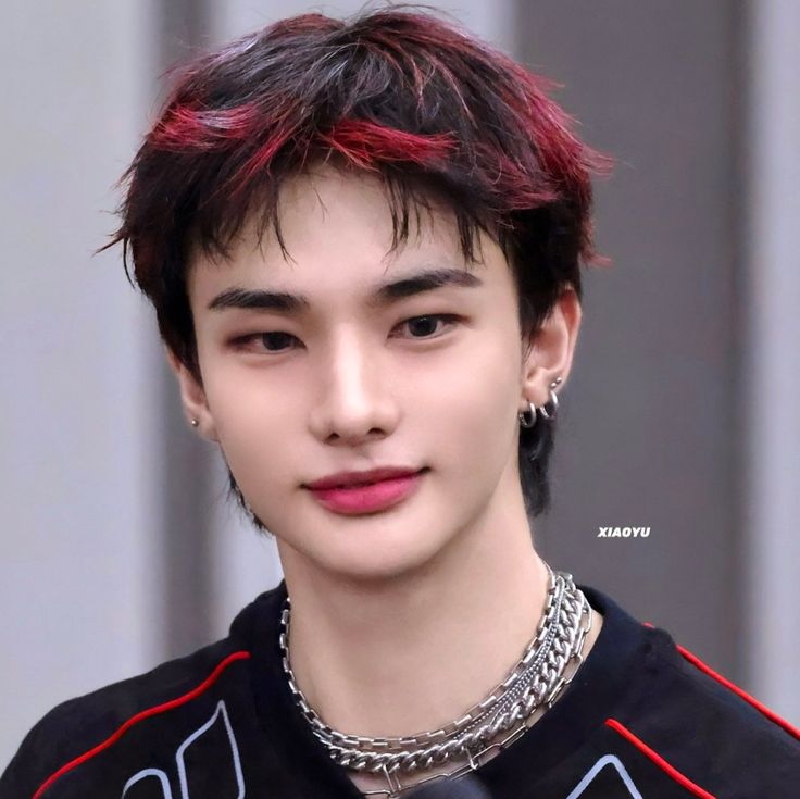 Close-up portrait of Hwang Hyunjin with red-highlighted dark hair and layered chain necklaces