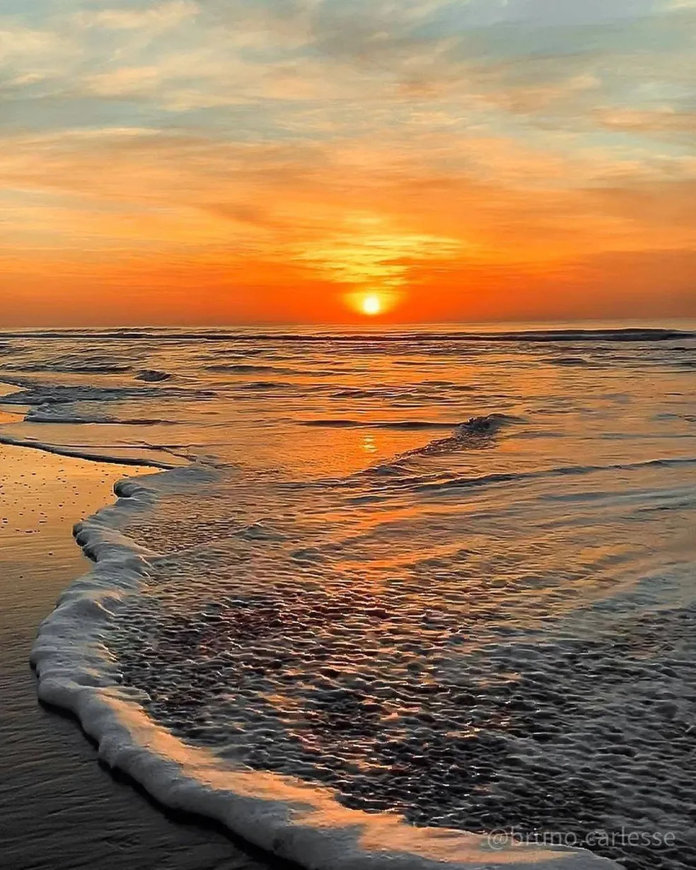 Sunset over the ocean with foamy waves on a sandy beach