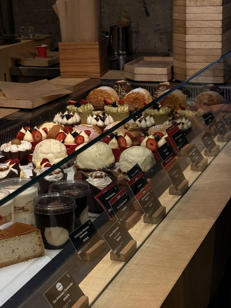 Glass display case in a café showing rows of cream-topped pastries, cakes, and assorted sweets with price tags