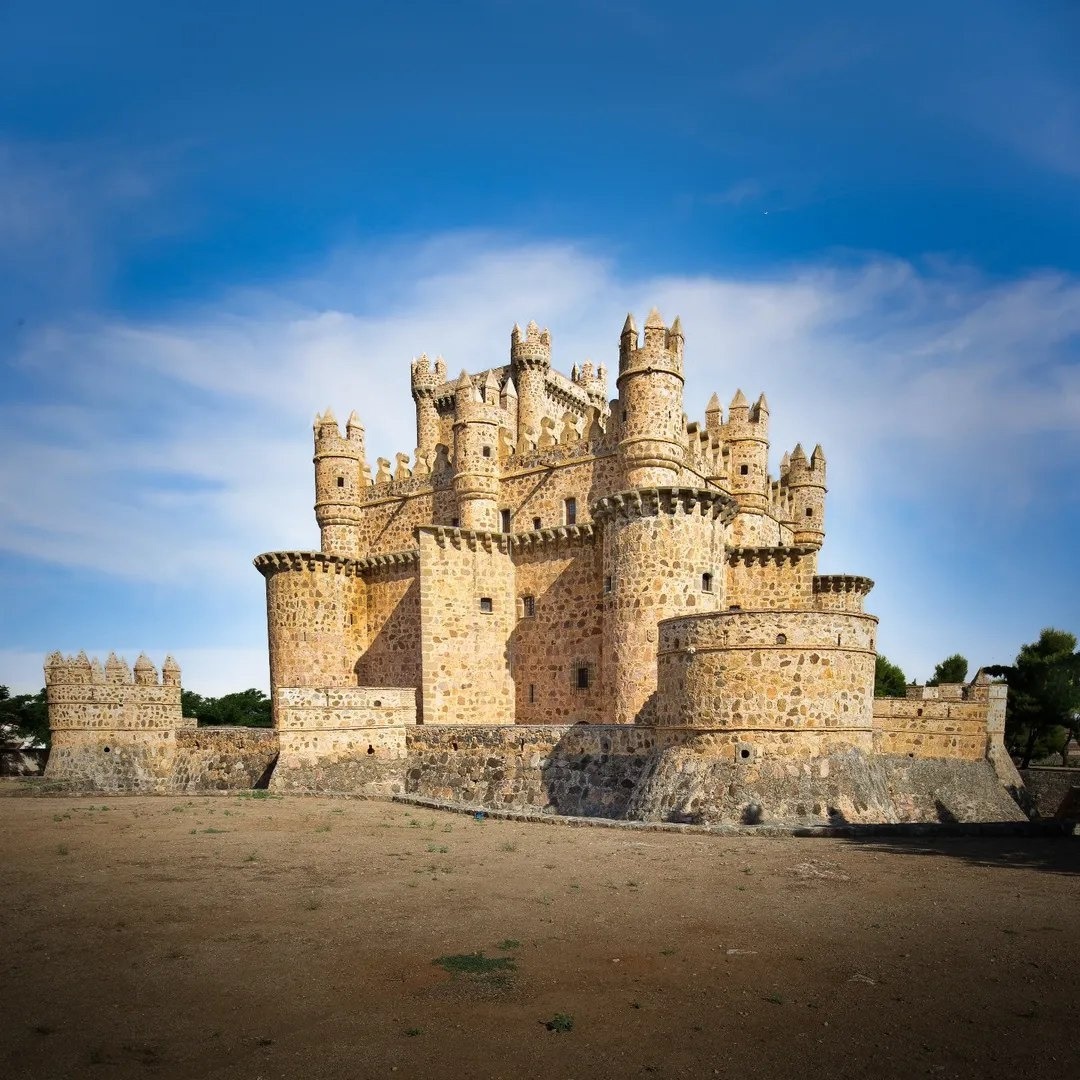 Medieval stone castle with cylindrical towers and crenellated walls against blue sky