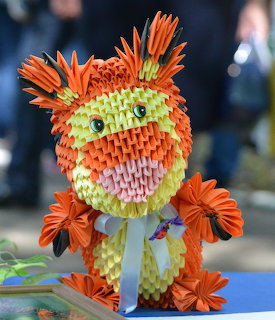 3D origami paper lion sculpture in orange, yellow, green and pink with decorative paper flowers
