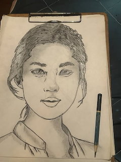 Pencil portrait sketch of a young woman on a clipboard with a pencil beside the paper