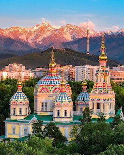 Colorful onion domes of Ascension Cathedral in Almaty with snow-capped mountains at sunset