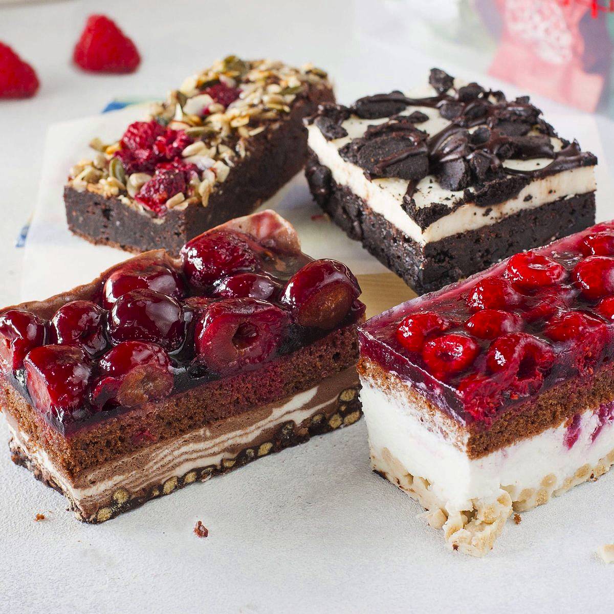 Four layered dessert bars with various toppings including berries, nuts, and chocolate on white marble