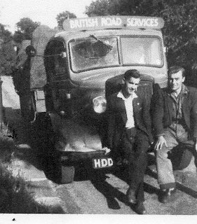 Vintage black and white photo of two men sitting on the front of a lorry by a country road