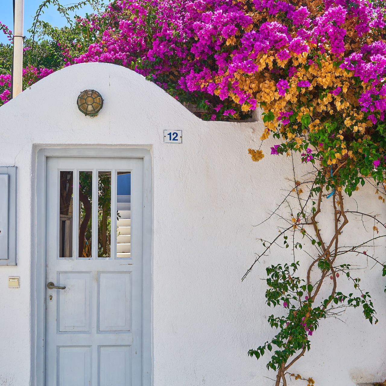 White Greek house entrance with vibrant purple bougainvillea and blue door