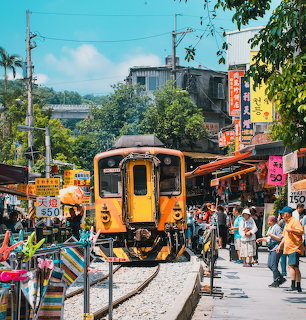 Yellow train moving through a crowded street market in Taiwan with shops and people on both sides