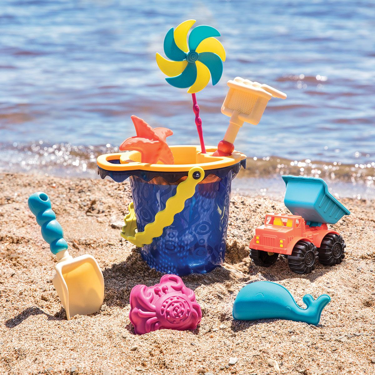 Colorful beach toys on sand by the water, with a bucket, shovel, toy truck, and pinwheel