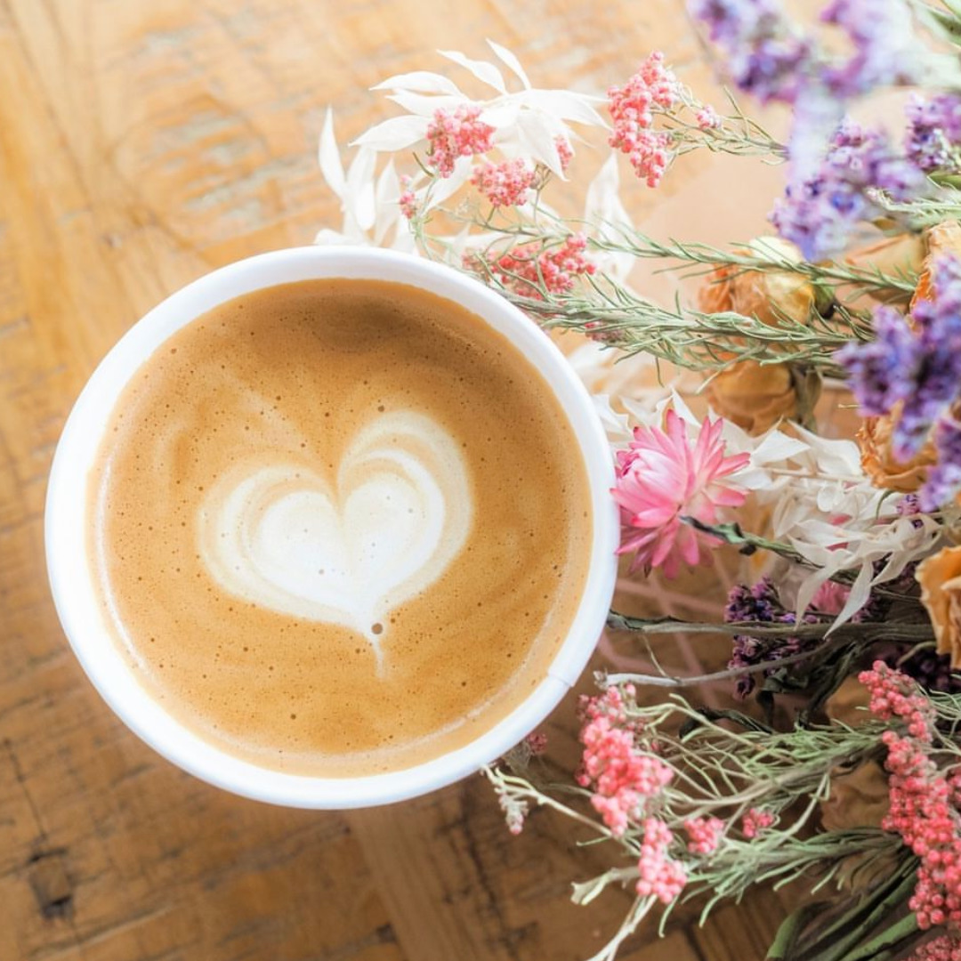 Top view of a latte with heart foam next to dried flowers on a wooden table