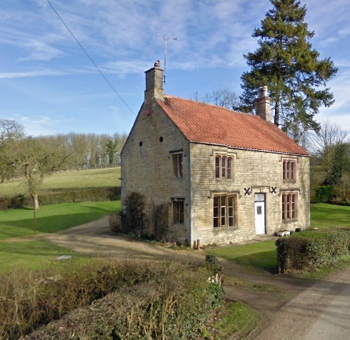 Two-story stone cottage with orange tile roof in rural green landscape