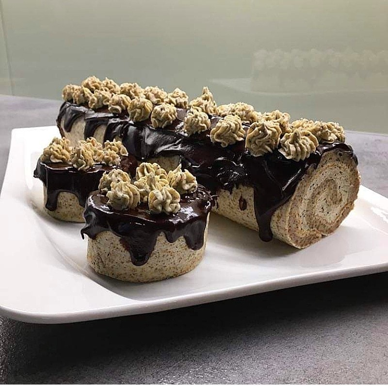 Three chocolate-glazed Swiss roll pastries with cream topping on a white plate