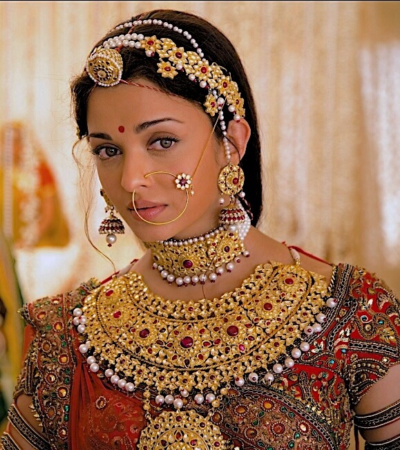 Woman wearing traditional Indian bridal jewelry including gold necklaces, nose ring, and embroidered outfit