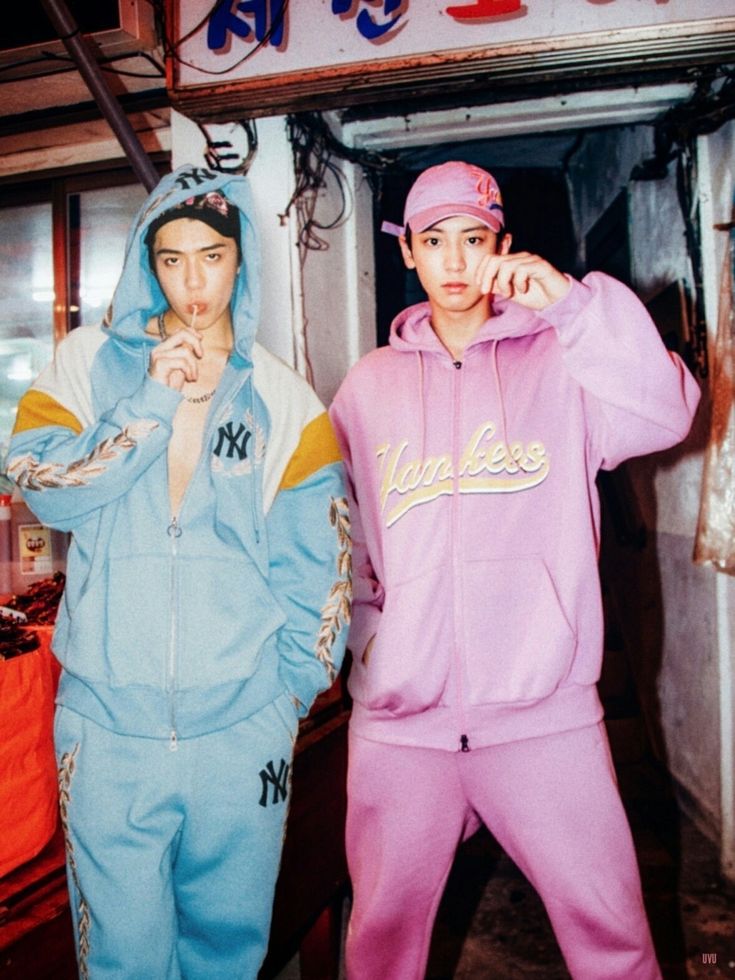 Two young men in blue and pink tracksuits posing in an industrial space