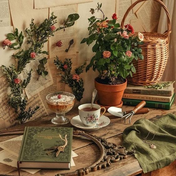 Rustic table with potted plants, teacup, books, wicker basket and green fabric in cottagecore style