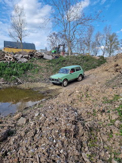 Green Lada Niva on a muddy slope near a puddle in a rural landscape