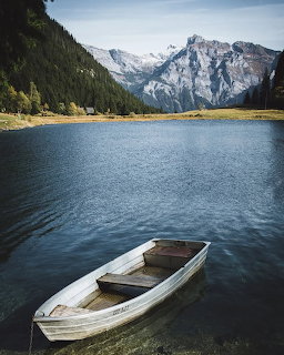 White rowboat on a calm alpine lake with snow-capped mountains and green forested slopes in background