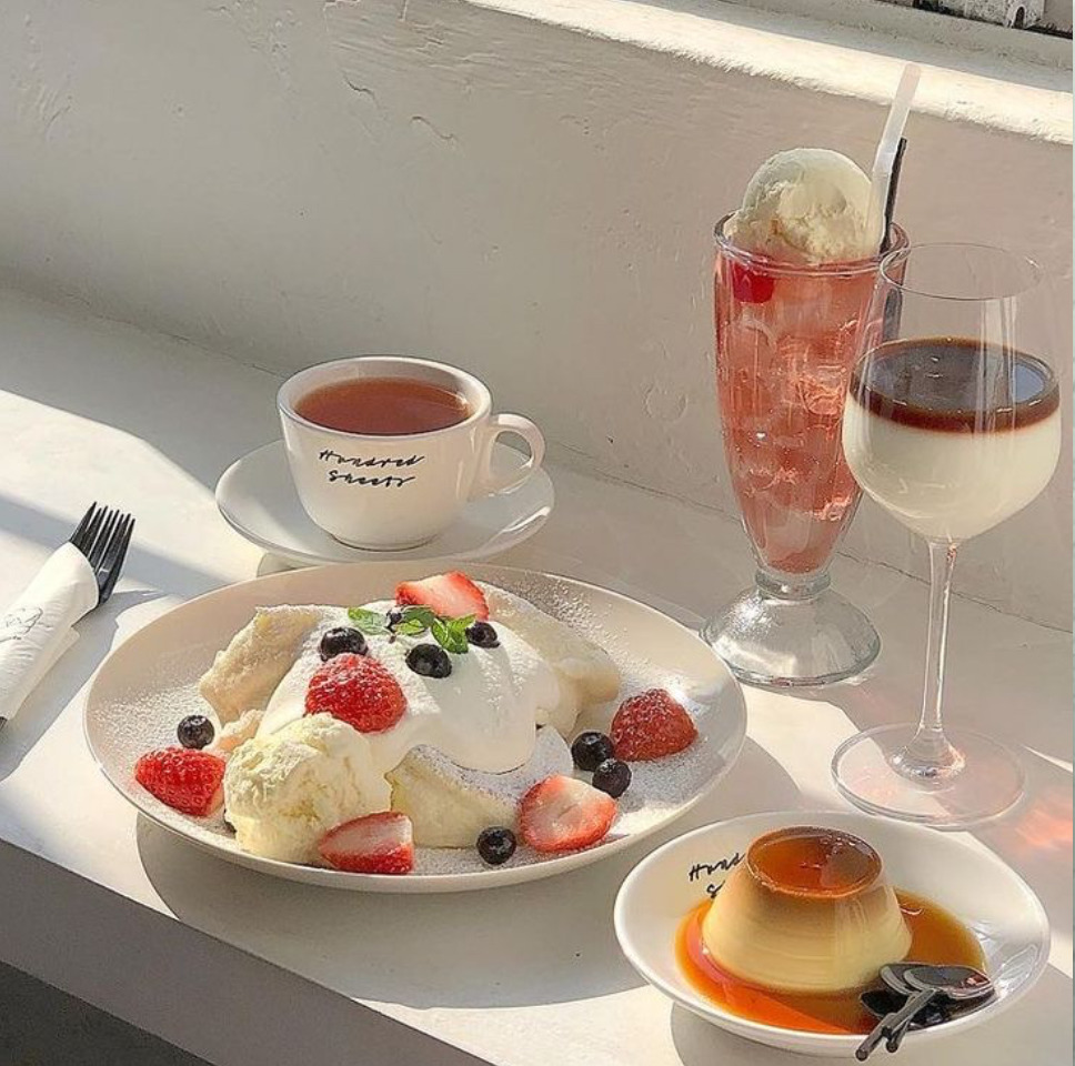 Dessert plate with berries and cream, coffee, wine glass, and pink cocktail on white table