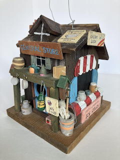 Rustic wooden birdhouse designed as a miniature general store with weathered signs and striped awning