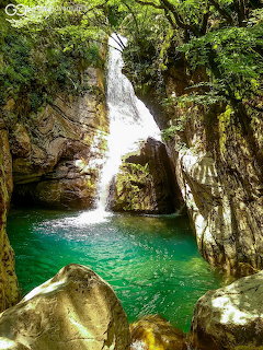 Waterfall cascading into a turquoise pool surrounded by rocks and green vegetation in a gorge