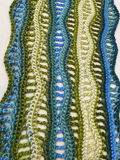 Crocheted scarf with wavy vertical stripes in blue, green, and cream colors