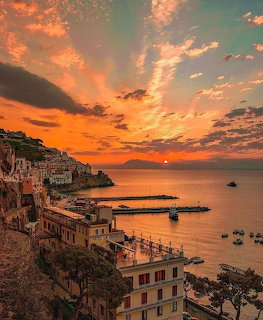 Sunset over a coastal village by a calm bay with boats and a small harbor