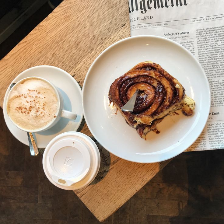 Cappuccino, cinnamon roll, and newspaper arranged on wooden table