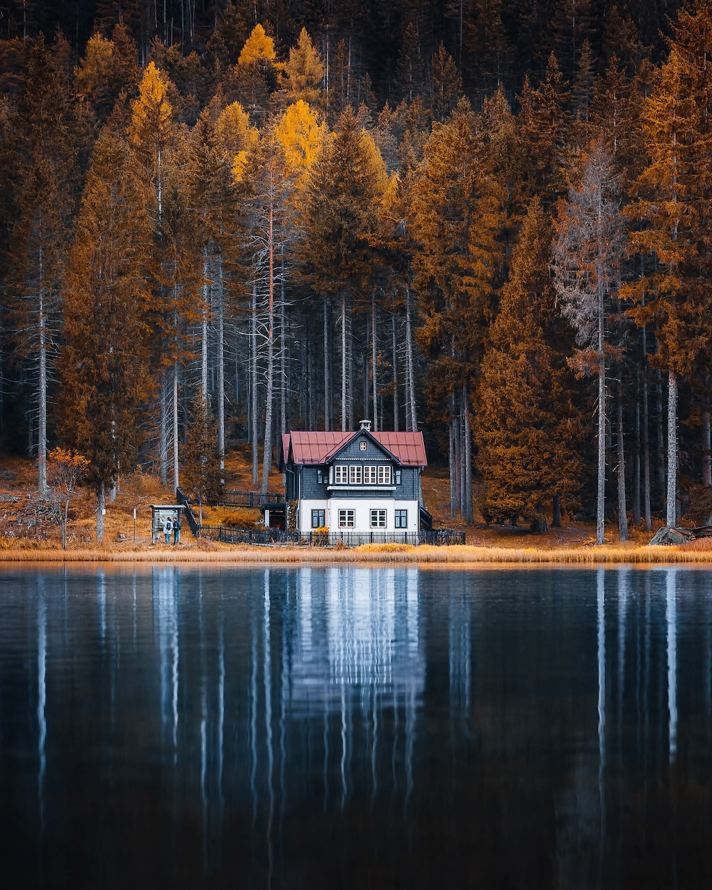 White house with red roof beside a still lake reflecting golden autumn forest