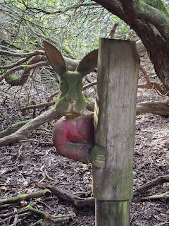 Colorful carved wooden hare sculpture on a post in a woodland setting with bare branches