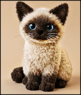 Crocheted amigurumi Siamese kitten with blue eyes and dark brown markings sitting upright