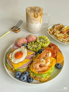 Breakfast plate with fried egg, kiwi, blueberries, pastries, waffle, and iced coffee on marble surface