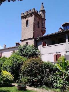 Medieval stone castle tower with crenellations rising above white buildings and green trees under blue sky