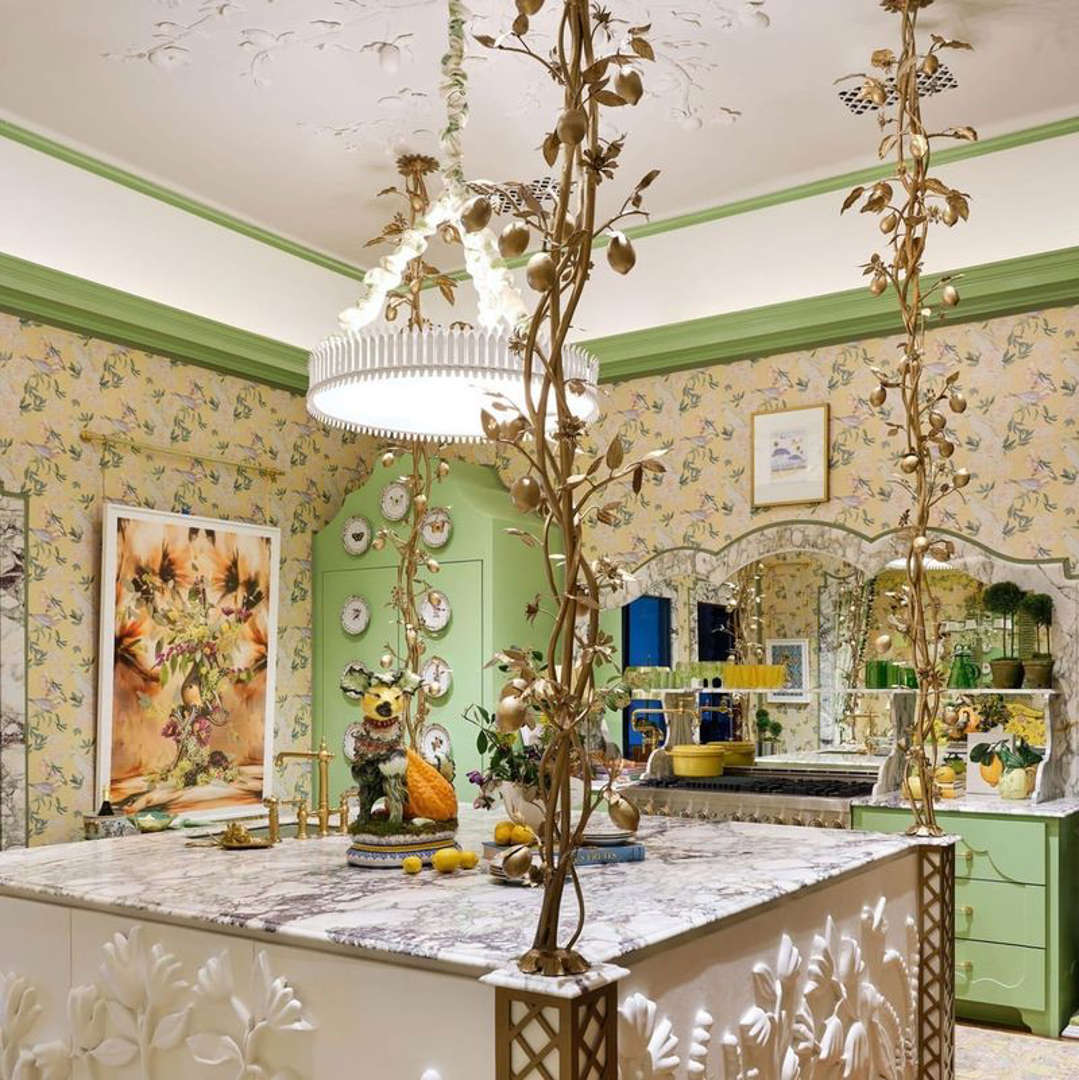 Ornate kitchen with floral wallpaper, gold branches, marble island, green trim and cabinets, crystal chandelier