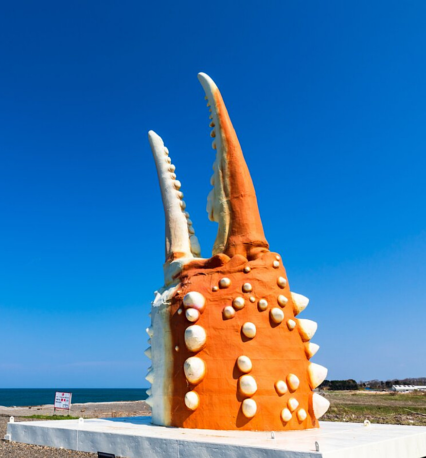 Large orange crab claw sculpture by the shore under a clear blue sky