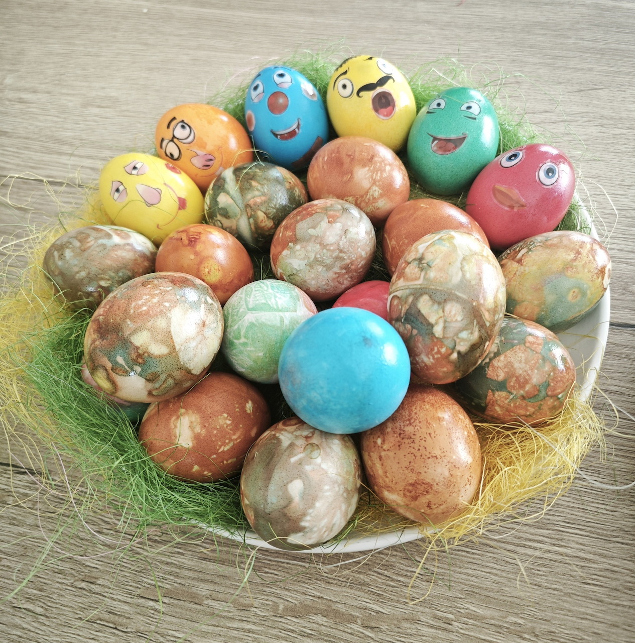 Bowl of colorful dyed Easter eggs, some painted with smiling faces, on a wooden table