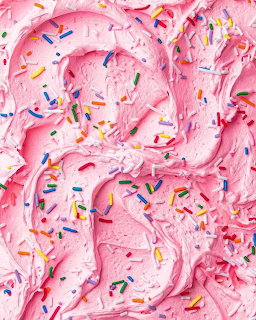 Swirled pink frosting with colorful sprinkles scattered across the surface