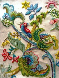 Detailed floral embroidery with vibrant flowers and scrolling vines on cream textile