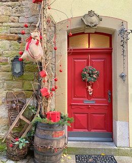 Red front door with Christmas wreath, rustic vines, lantern, and holiday decorations outside a stone wall