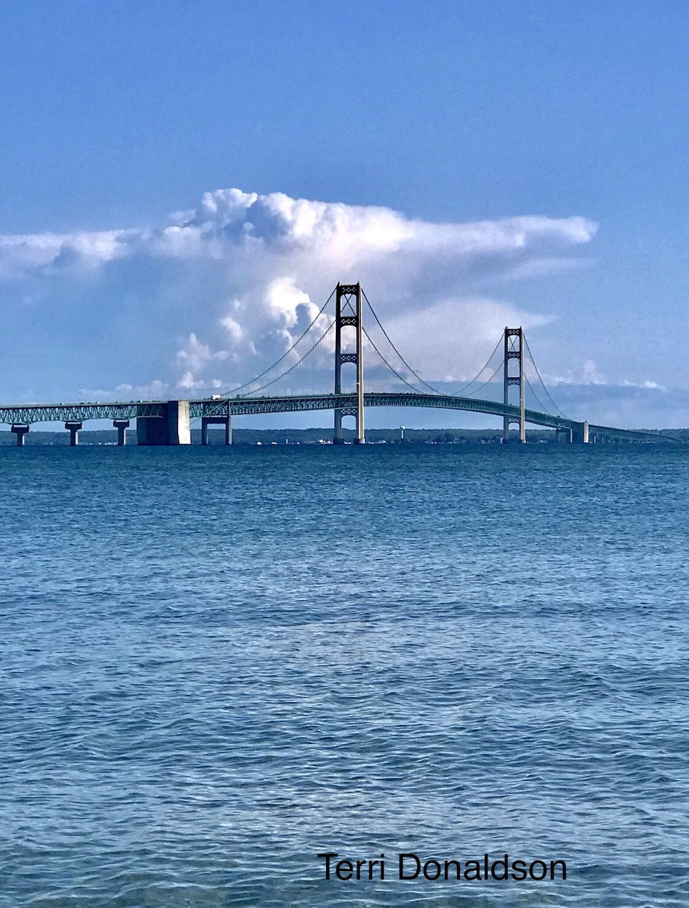 Suspension bridge over blue water under a large white cloud