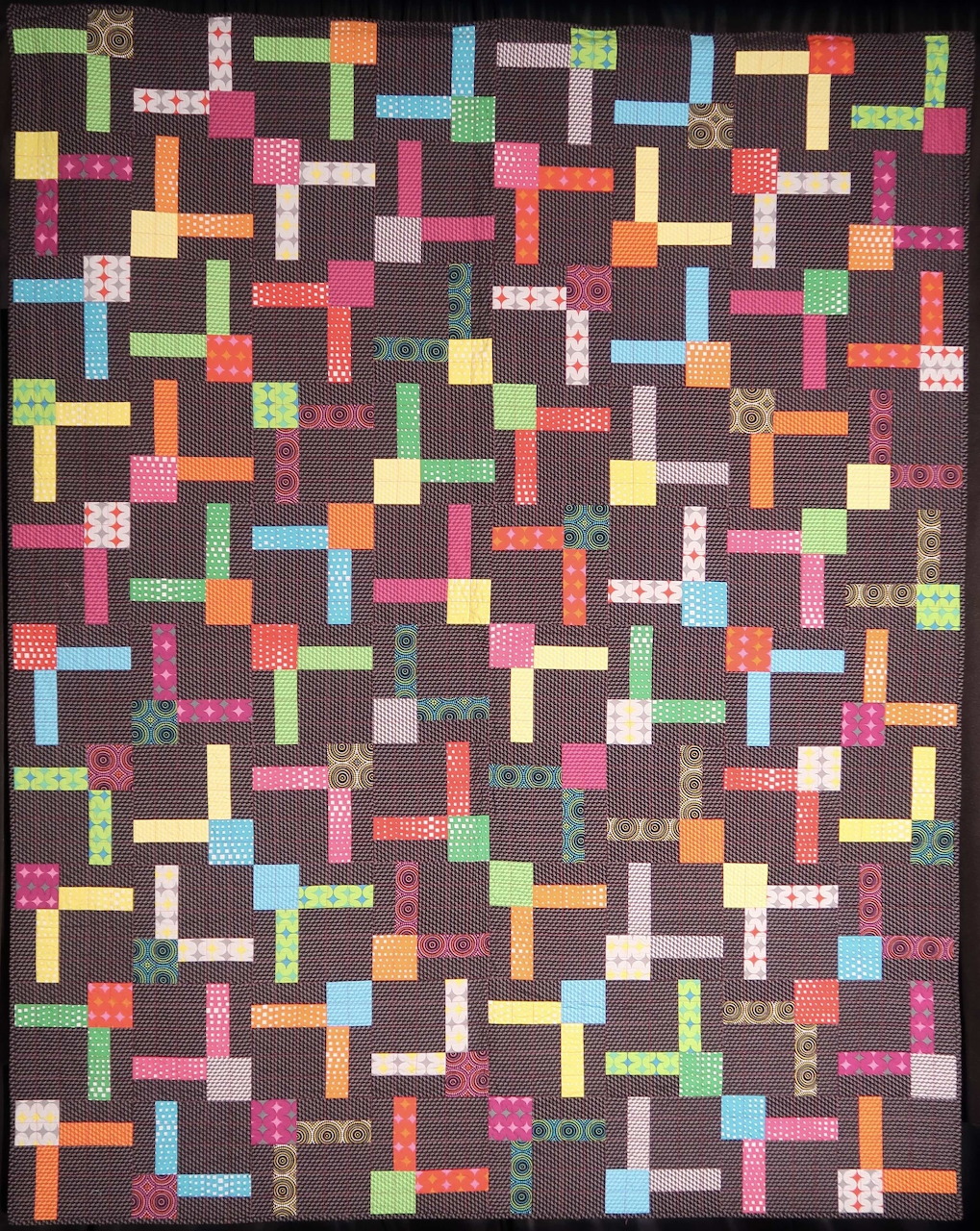 Colorful patchwork quilt with interlocking rectangular blocks in varied fabrics on dark background