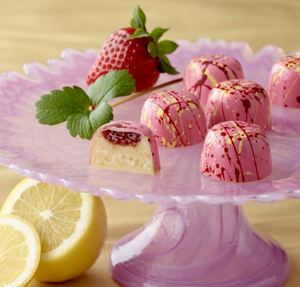 Pink chocolate truffles with gold flakes on pink cake stand with strawberry and lemon