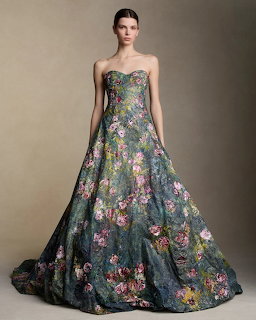 Model in a strapless green floral ball gown posing against a grey background