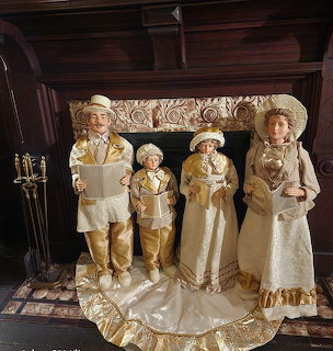 Four porcelain Christmas caroler figurines in Victorian clothing holding songbooks on lace doily